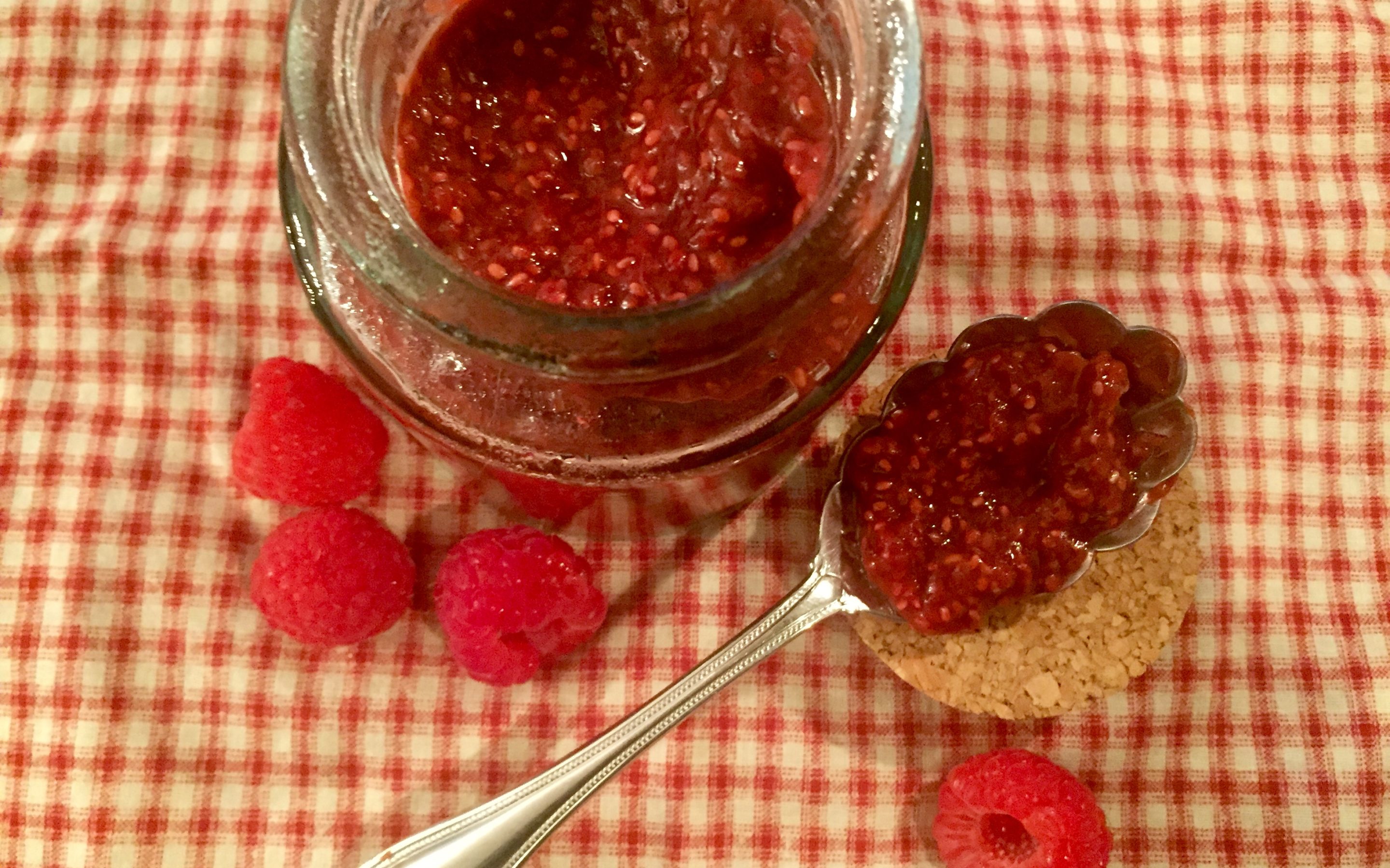 home made raspberry jam with a spoon and raspberries