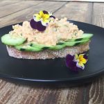 Smashed buffalo chickpea salad on cucumbers on a piece of toast with flowers