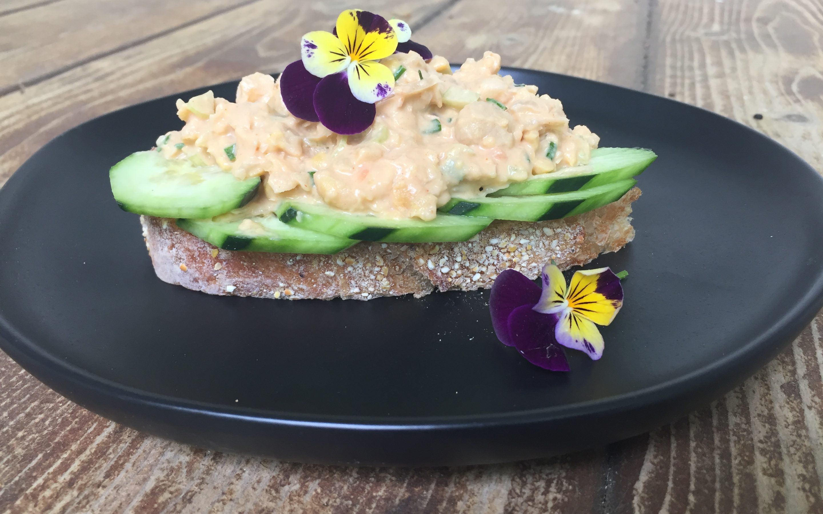 Smashed buffalo chickpea salad on cucumbers on a piece of toast with flowers