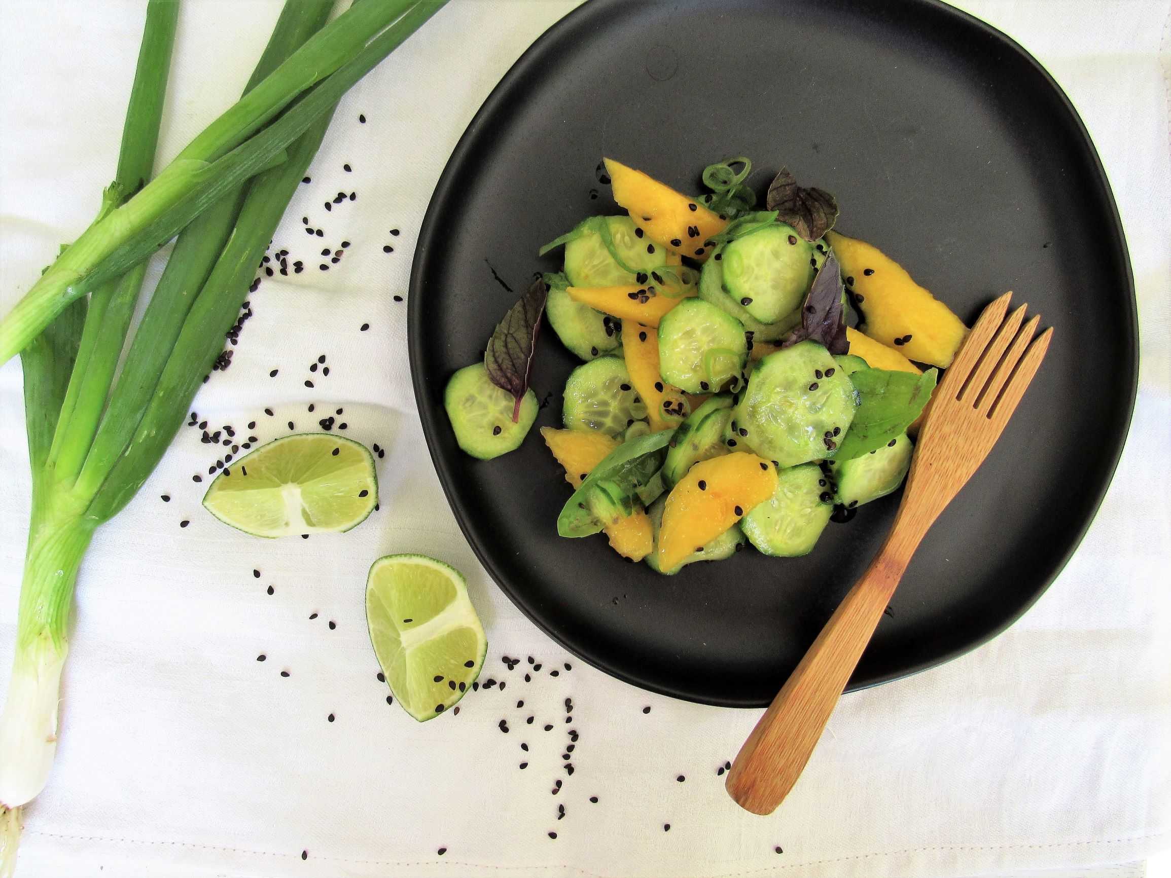 Thai cucumber and mango salad on a black plate with a bamboo fork