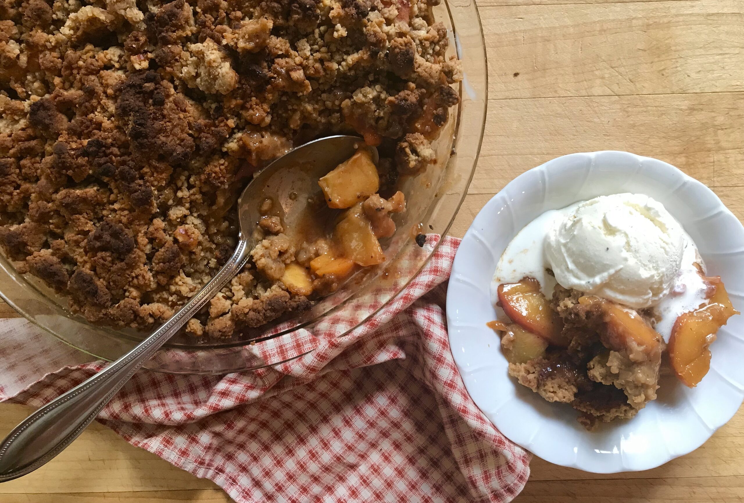 pecan peach crumble in a pie dish and in a white bowl served with ice cream