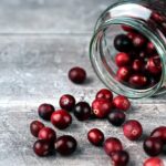 clear glass jar with cranberries spilling out on a grey counter. Photo by Rasa Kasparaviciene on Unsplash